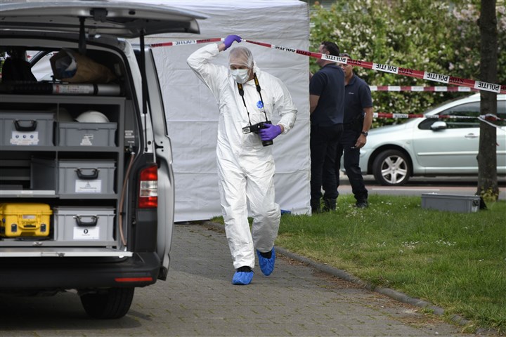 Police officers and forensic investigator in protective clothing and face mask, at screened-off area where someone was murdered