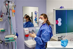 Verpleegkundige met mondkapje en gezichtsbescherming voor de spiegel in de quarantainekamer van een ziekenhuis