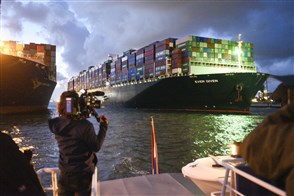 Containerschip Ever Given komt aan bij containerterminal. Op voorgrond persoon met camera.