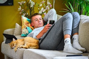 Jongen, puber hangt chill op de bank en is op zijn telefoon aan het kijken naar snapchat en instagram.