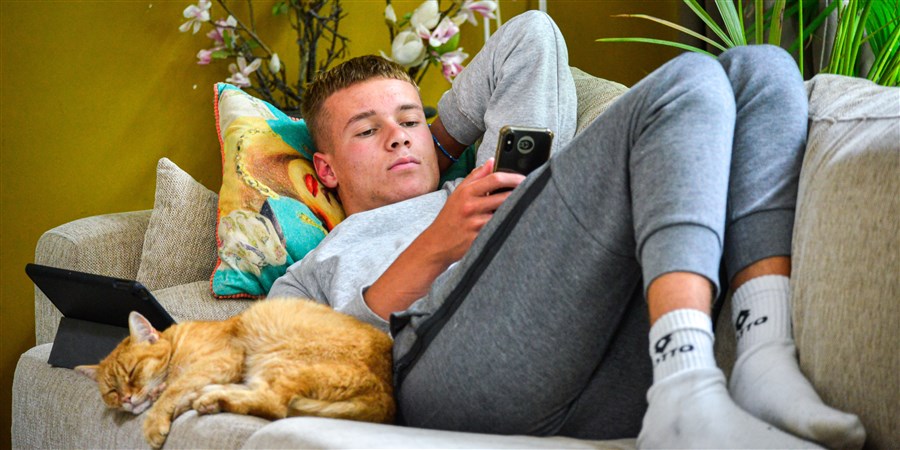 Jongen, puber hangt chill op de bank en is op zijn telefoon aan het kijken naar snapchat en instagram.