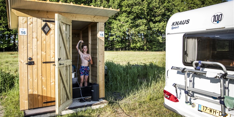 Jongen neemt douche op camping in apart toiletgebouwtje, naast caravan.