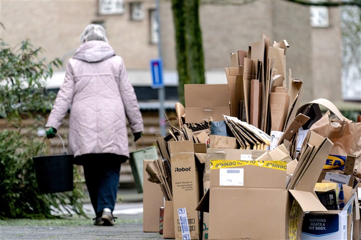 Vrouw loopt langs een enorme hoeveelheid kartonnen dozen die langs de straat is gezet om opgehaald te worden