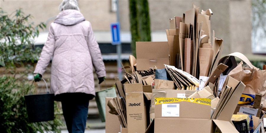 Vrouw loopt langs een enorme hoeveelheid kartonnen dozen die langs de straat is gezet om opgehaald te worden