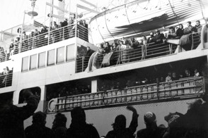 Een schip met emigranten begin 1956. De achterblijvers op de kade zwaaien als afscheid van de vertrekkende familie.