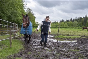 Meisje met haar paard aan een touw lopen door een modderige wei.