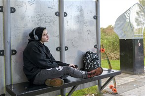 Jonge meid in zwarte kleding hangt alleen op bankje in een park, depressief en in gedachten.