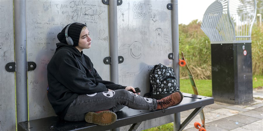 Jonge meid in zwarte kleding hangt alleen op bankje in een park, depressief en in gedachten.