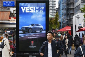 Mensen lopen langs billboard met advertentie voor een Chinees automerk.
