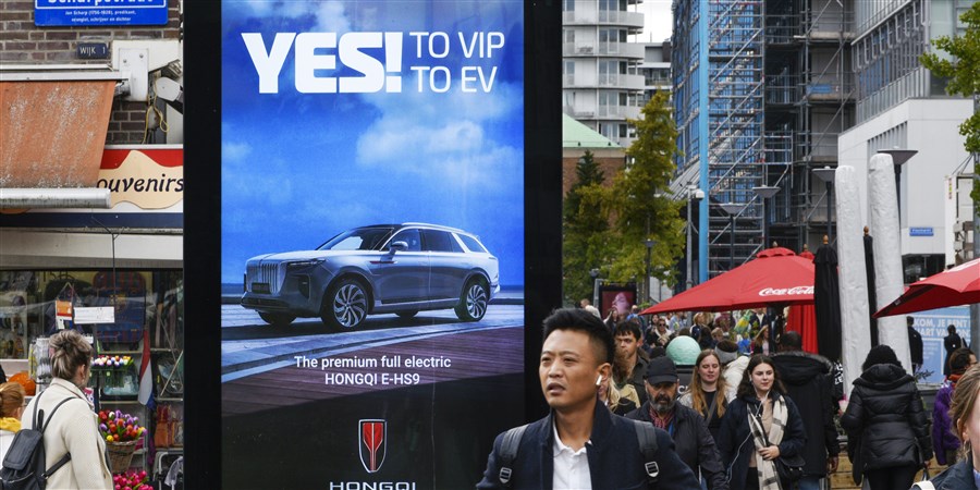 Mensen lopen langs billboard met advertentie voor een Chinees automerk.