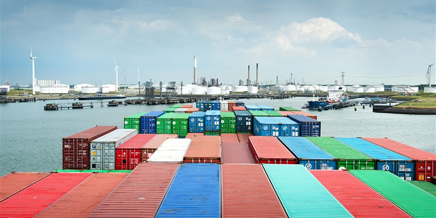 Containerschip vaart haven binnen, op de achtergrond opslagtanks en windmolens