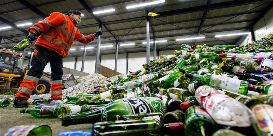 Een medewerker van een glasrecyclingbedrijf verwerkt een enorme hoeveelheid flessen.