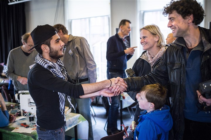 Vluchtelingen uit Syrie werken mee in het Repair Cafe in de stad Groningen. Een syrische jongen schut een nederlands gezin de hand.