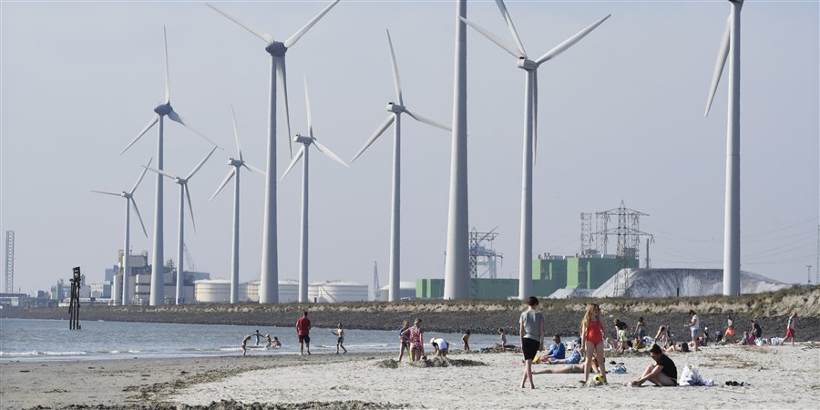 Klein recreatiestrand met windmolens en industriegebied op de achtergrond