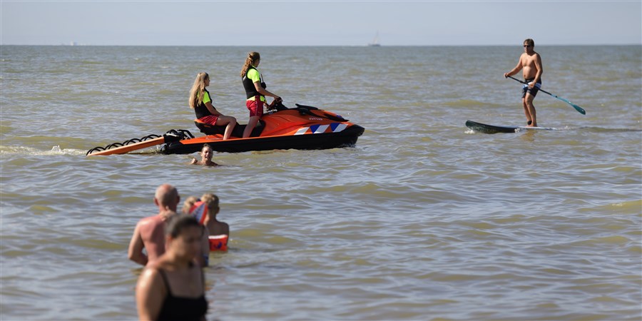 Twee leden van de reddingsbrigade op een jetski van de Reddingsbrigade spreken een man aan op een supboard.