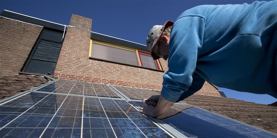 Man monteert zonnepanelen op het dak van een woning