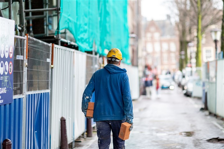 een bouwvakker die met bakstenen in zijn handen loopt