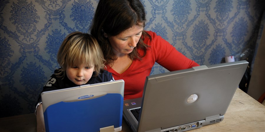 Vrouw met kind aan tafel achter laptop