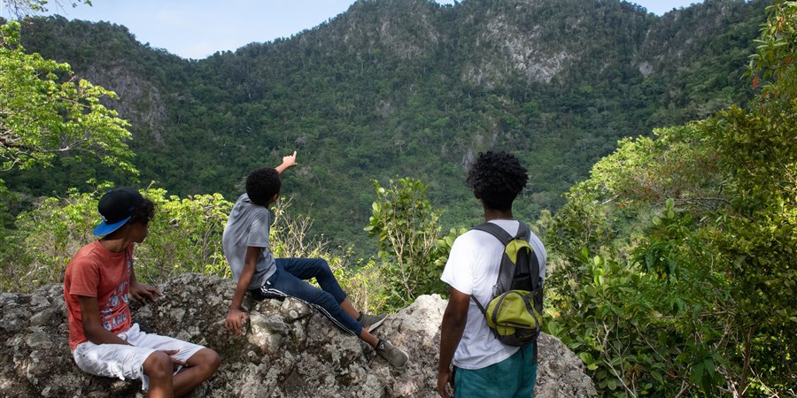 Jongeren zitten op een rots en kijken in de verte. Een jongere wijst in de verte