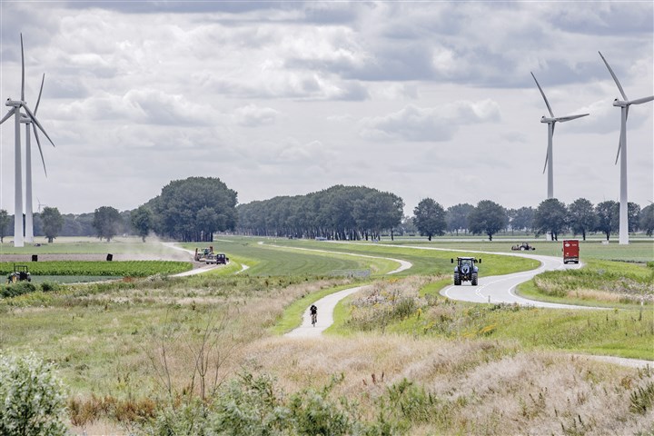 Landschap in Flevoland met windmolens, fietser, vrachtwagen, tractor en boer die mest uitrijdt.