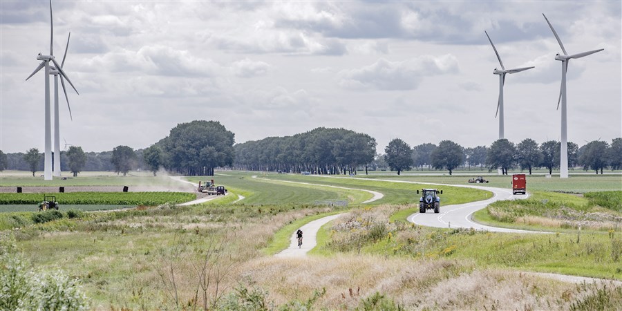 Landschap in Flevoland met windmolens, fietser, vrachtwagen, tractor en boer die mest uitrijdt.