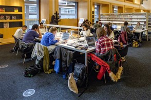 Studenten zitten achter hun laptops aan grote tafel in de bibliotheek.
