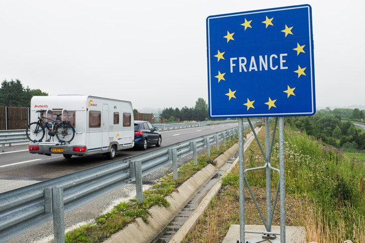 Nederlandse auto met caravan rijdt de grens van Belgie naar Frankrijk over.