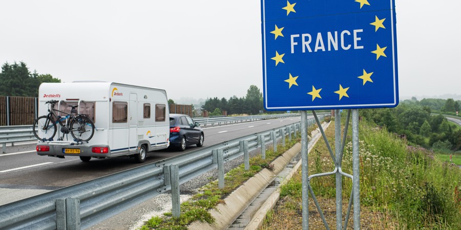 Nederlandse auto met caravan rijdt de grens van Belgie naar Frankrijk over.