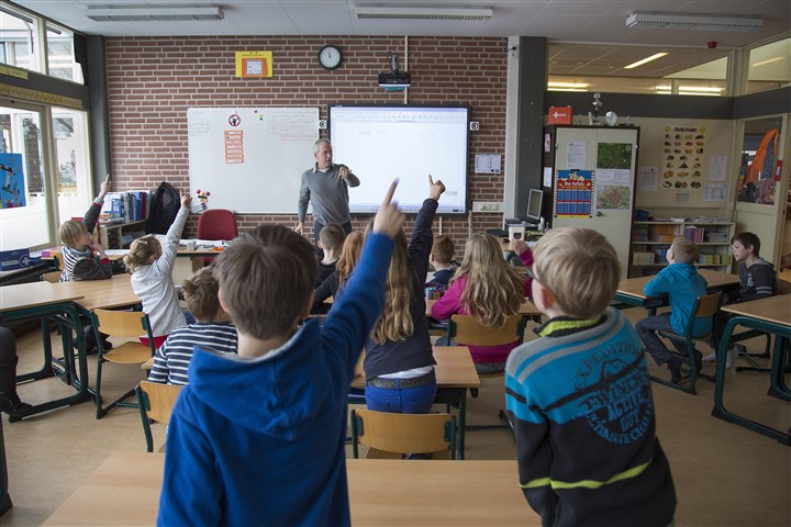 Leraar staat voor de klas en de kinderen hebben hun hand omhoog