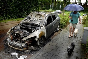 Vrouw loopt met honden langs afgebrande auto