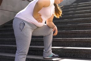 Een zomers geklede vrouw met overgewicht rust uit uit op de treden van een trap.
