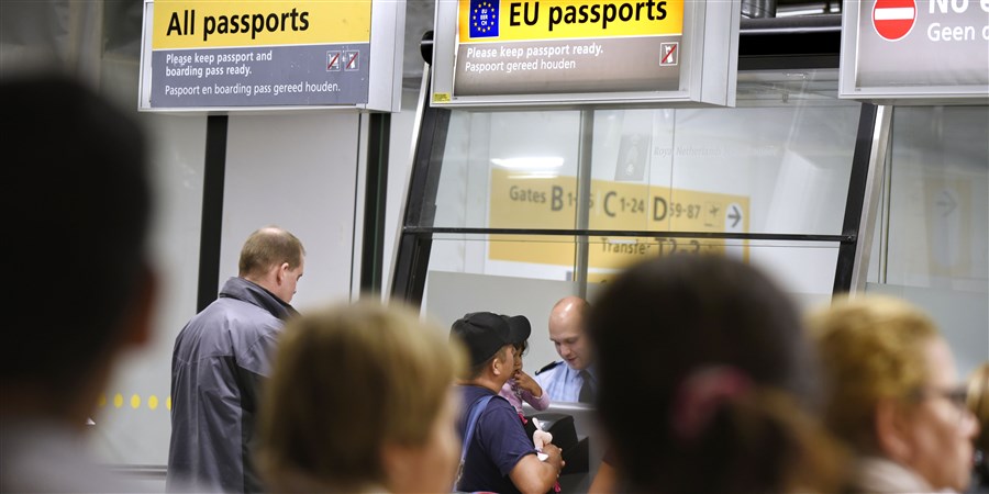 Travellers waiting in front of the passport control desk at Amsterdam Schiphol Airport