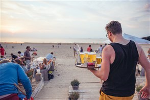 Kelner met drankjes op terras aan het strand