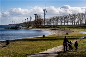 Moeder met 2 kinderen wandelen langs water waar windmolens en bomen langs staan