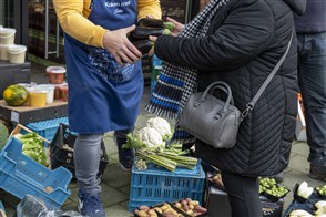 Een vrouw koopt aubergines bij een  groentewinkel, waar de verse groente buiten ligt uitgestald
