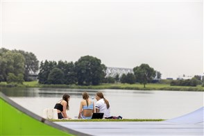 Vrouwen zitten bij een steiger in het gras bij een recreatieplas