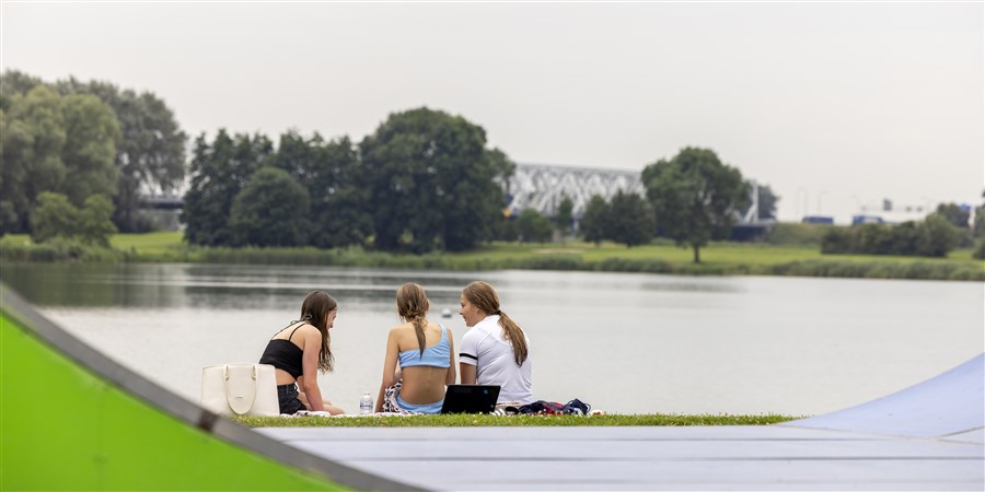 Vrouwen zitten bij een steiger in het gras bij een recreatieplas