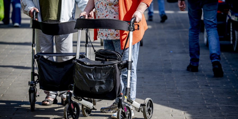 Oudere man en vrouw achter een rollator op straat.